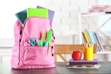 Backpack with school stationery on table indoors