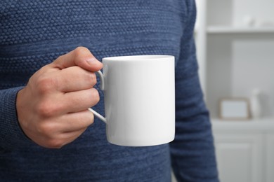 Photo of Man holding white mug at home, closeup. Mockup for design