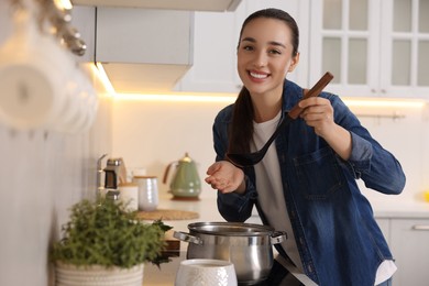 Smiling woman with ladle cooking soup in kitchen