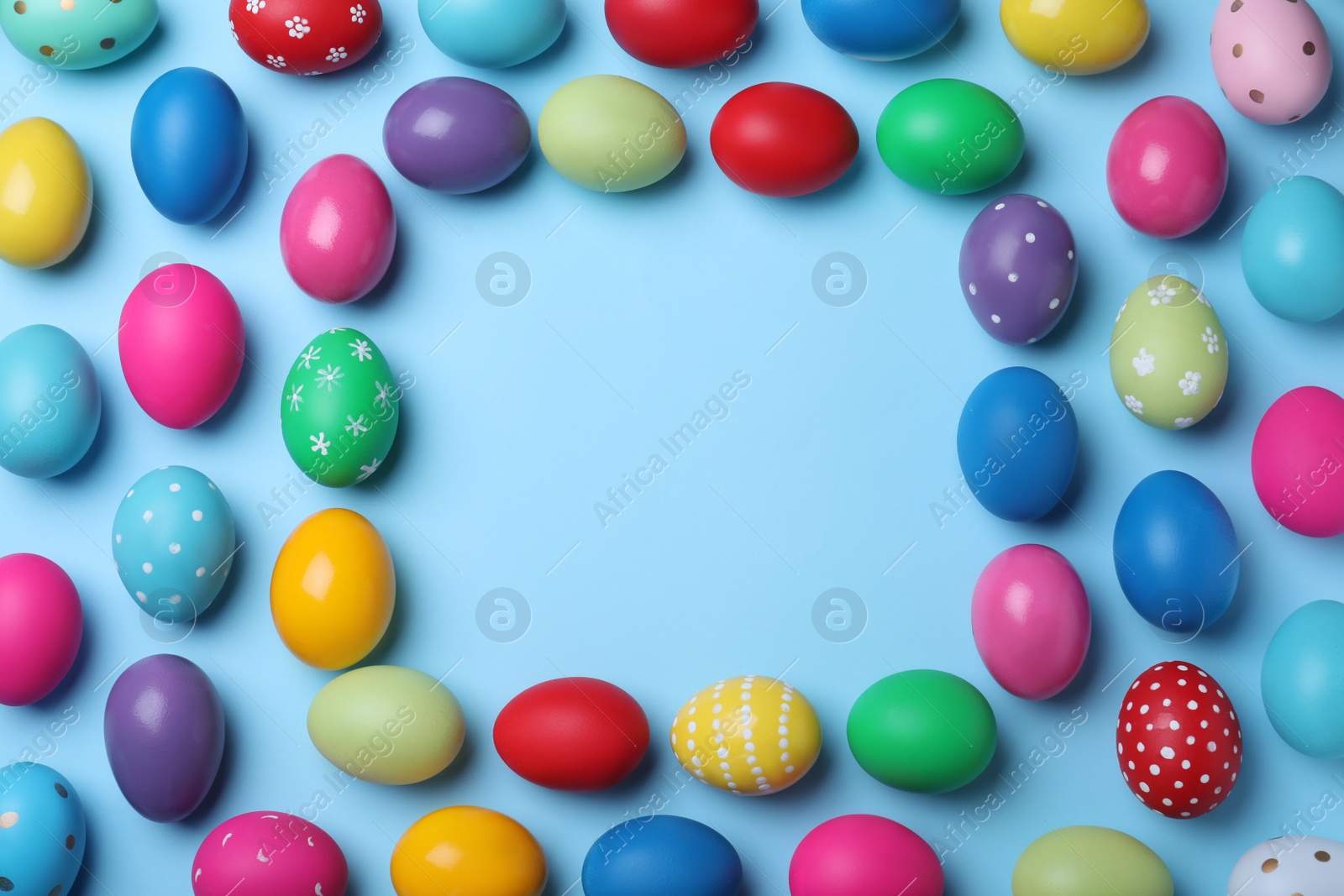 Photo of Frame of bright painted eggs on light blue background, top view with space for text. Happy Easter