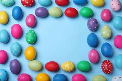 Photo of Frame of bright painted eggs on light blue background, top view with space for text. Happy Easter