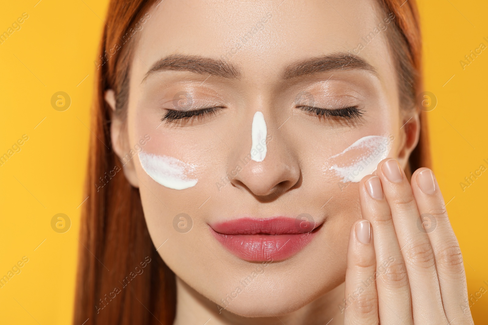 Photo of Beautiful young woman with sun protection cream on her face against orange background, closeup