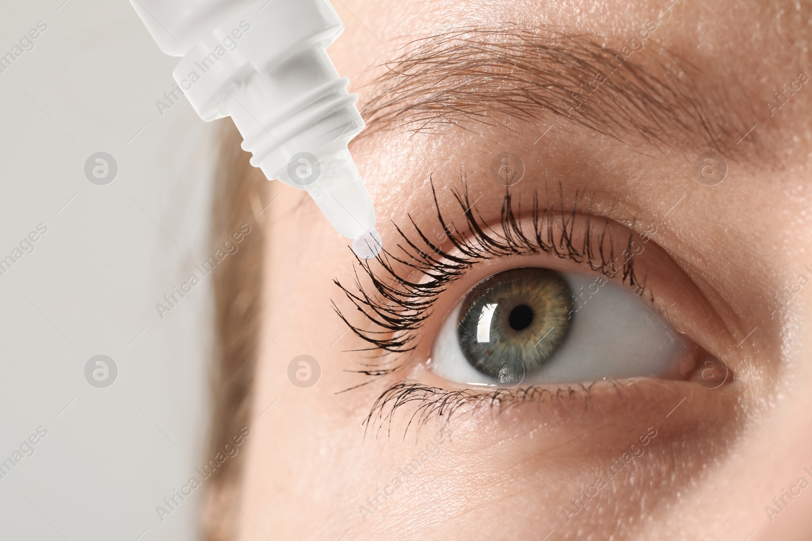 Image of Woman applying eye drops on light background, closeup