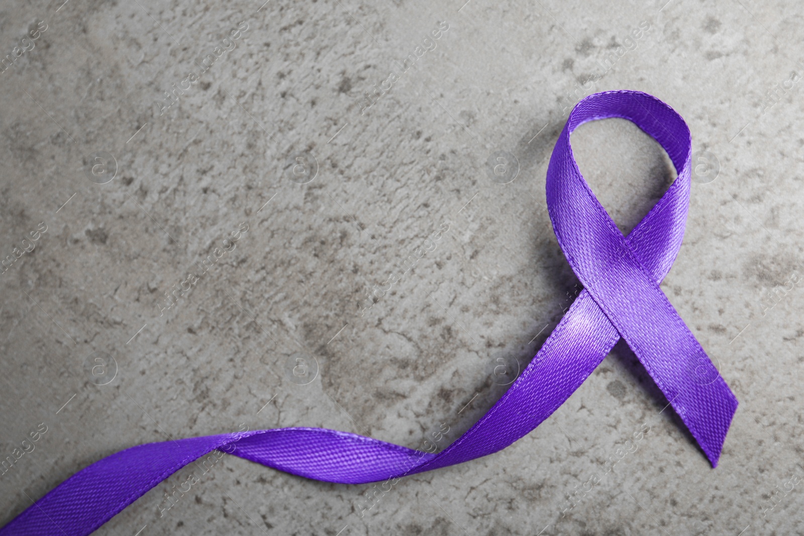 Photo of Purple ribbon on grey stone background, top view. Domestic violence awareness