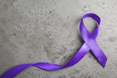 Purple ribbon on grey stone background, top view. Domestic violence awareness