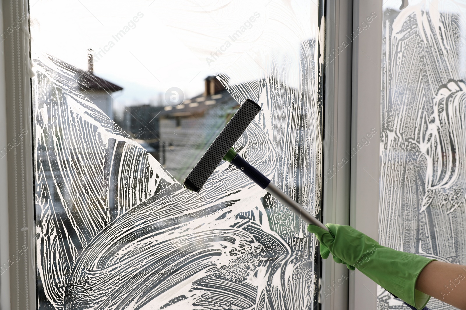 Photo of Woman cleaning window with squeegee indoors, closeup