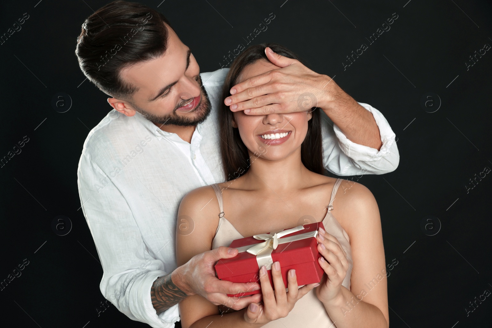 Photo of Man presenting gift to his girlfriend on black background