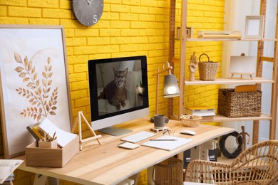 Stylish home office interior with comfortable workplace near yellow brick wall