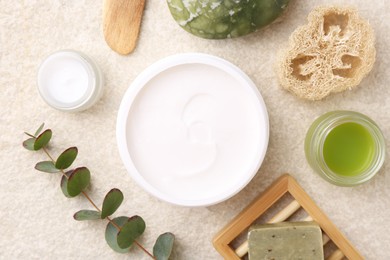 Photo of Flat lay composition with moisturizing cream in open jar and other body care products on light textured table