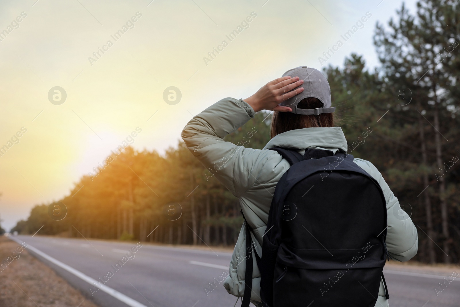 Photo of Woman with backpack on road near forest, back view