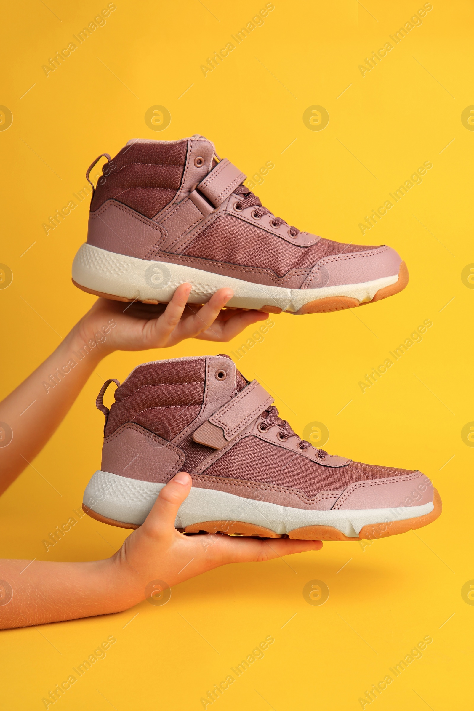 Photo of Girl holding stylish sneakers on yellow background, closeup