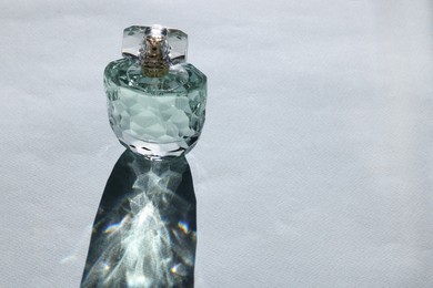 Photo of Luxury women's perfume. Sunlit glass bottle on grey background. Space for text