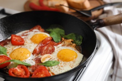 Delicious fried eggs with bacon and tomatoes in pan, closeup