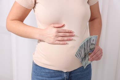 Photo of Surrogate mother. Pregnant woman with dollar banknotes indoors, closeup