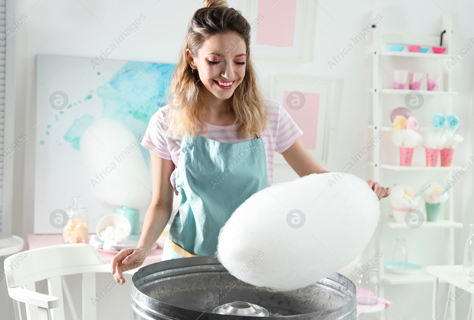 Photo of Young woman making cotton candy using modern machine in room