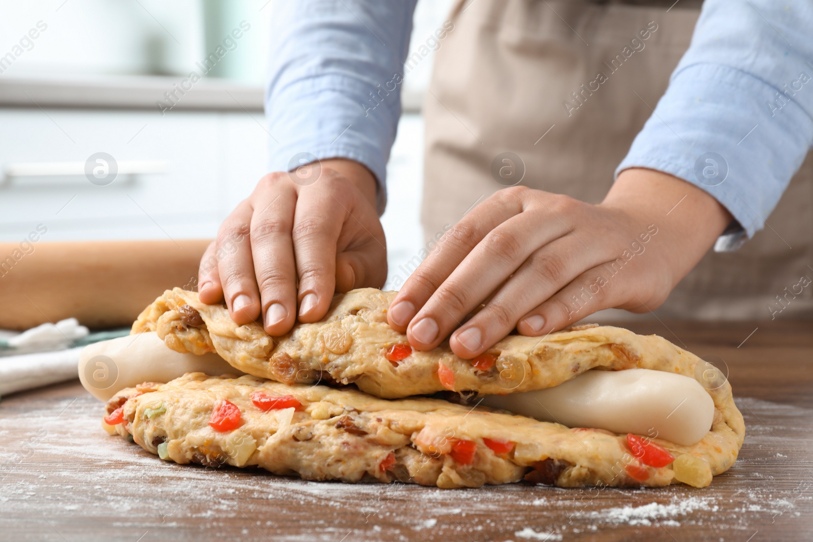 Photo of Woman putting marzipan into raw dough for Stollen at wooden table, closeup. Baking traditional German Christmas bread