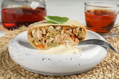 Photo of Piece of strudel with chicken, vegetables, sauce and tea on wicker mat, closeup