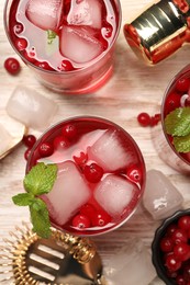 Photo of Tasty cranberry cocktail with ice cubes in glasses and bartender's tools on wooden table, flat lay
