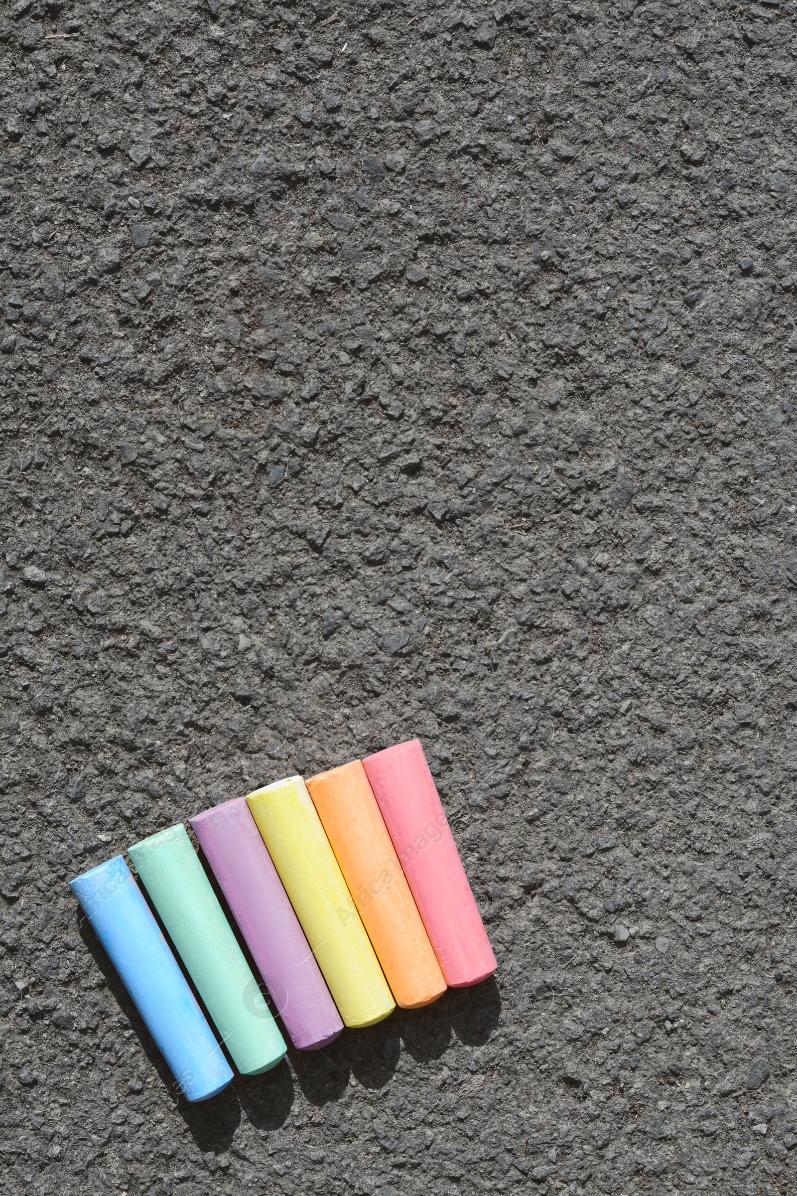 Photo of Colorful chalk sticks on asphalt, flat lay. Space for text