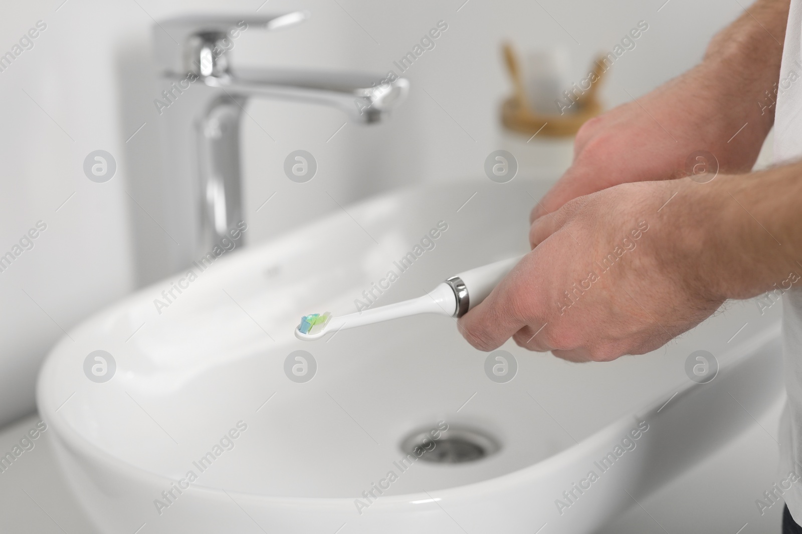 Photo of Man holding electric toothbrush near sink in bathroom, closeup