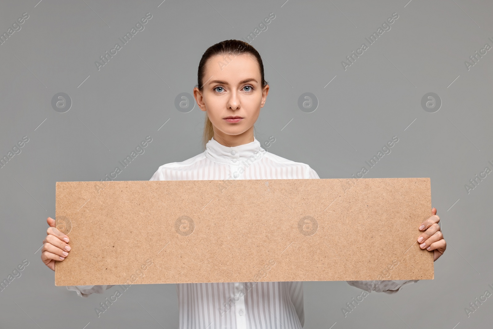 Photo of Woman holding blank cardboard banner on grey background, space for text