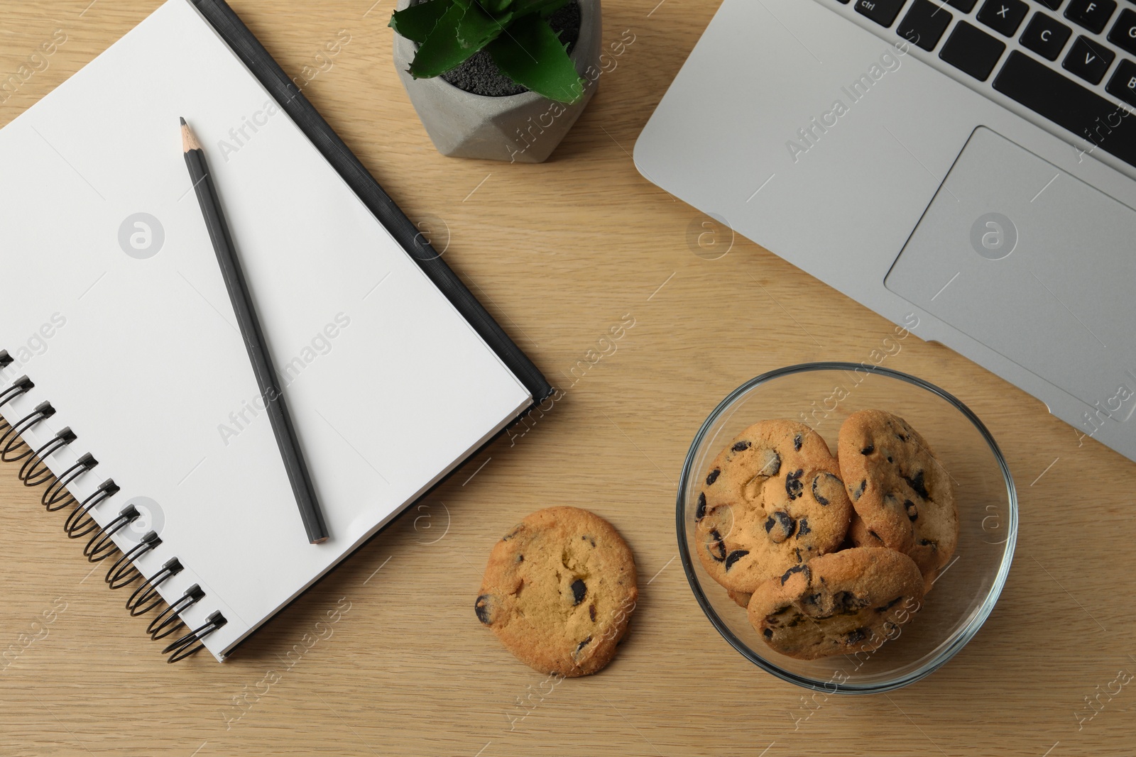 Photo of Chocolate chip cookies, notebook and laptop on wooden table at workplace, flat lay