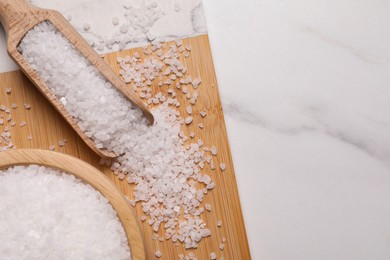 Photo of Wooden board with natural sea salt in scoop and bowl on white marble table, flat lay