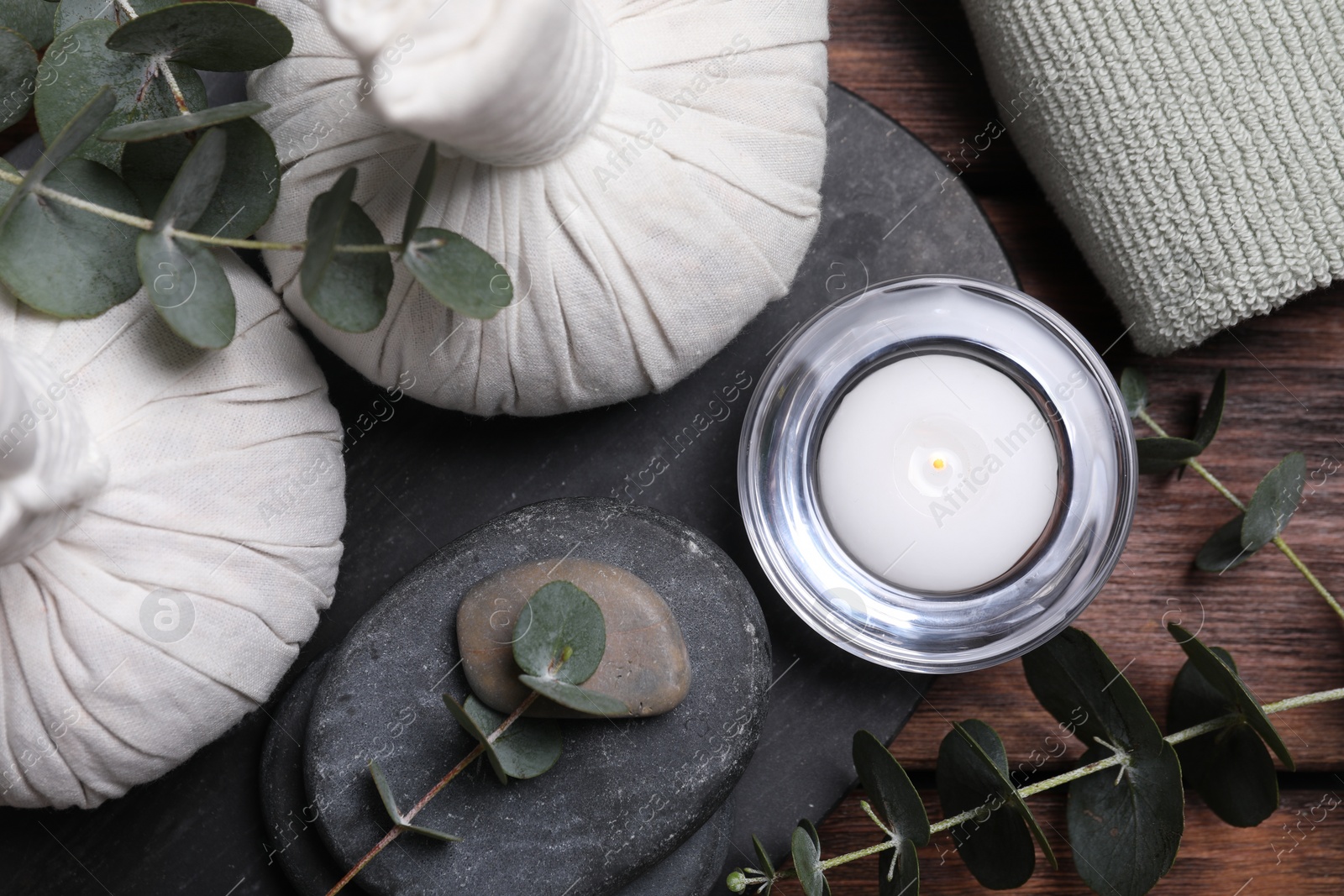 Photo of Beautiful spa composition with herbal massage bags, stones and eucalyptus branches on wooden table, flat lay