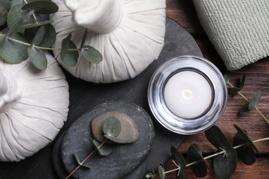 Beautiful spa composition with herbal massage bags, stones and eucalyptus branches on wooden table, flat lay