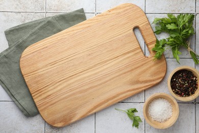 Photo of Cutting board, salt, pepper and parsley on white tiled table, flat lay. Space for text