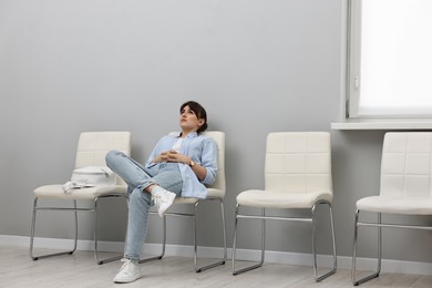 Photo of Woman sitting on chair and waiting for appointment indoors