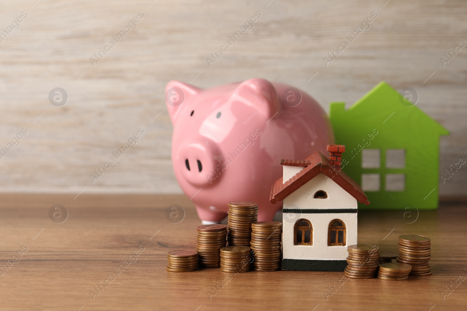 Photo of House models, piggy bank and stacked coins on wooden table, selective focus. Space for text