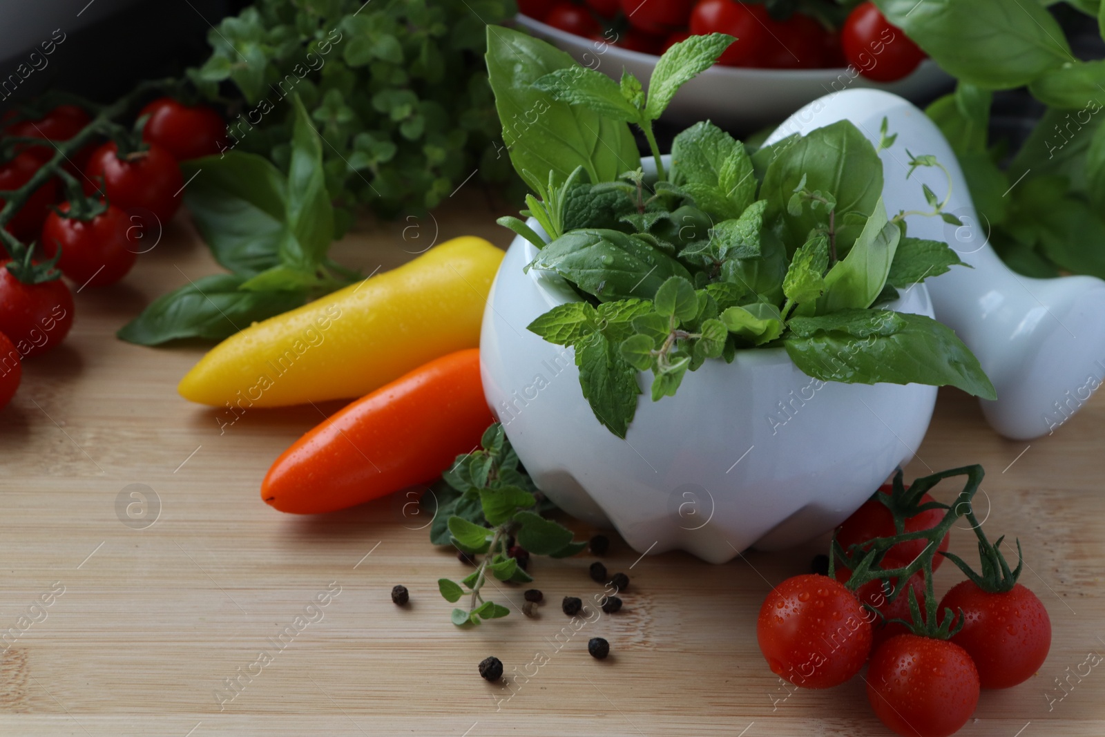 Photo of Mortar with different fresh herbs and pepper on wooden table, closeup