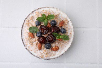 Tasty wheat porridge with milk, dates, blueberries and almonds in bowl on white table, top view
