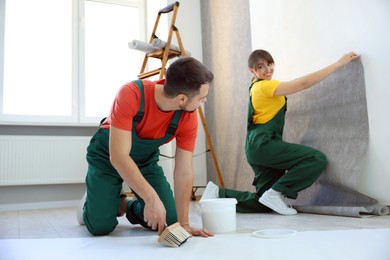 Photo of Workers hanging stylish gray wallpaper in room