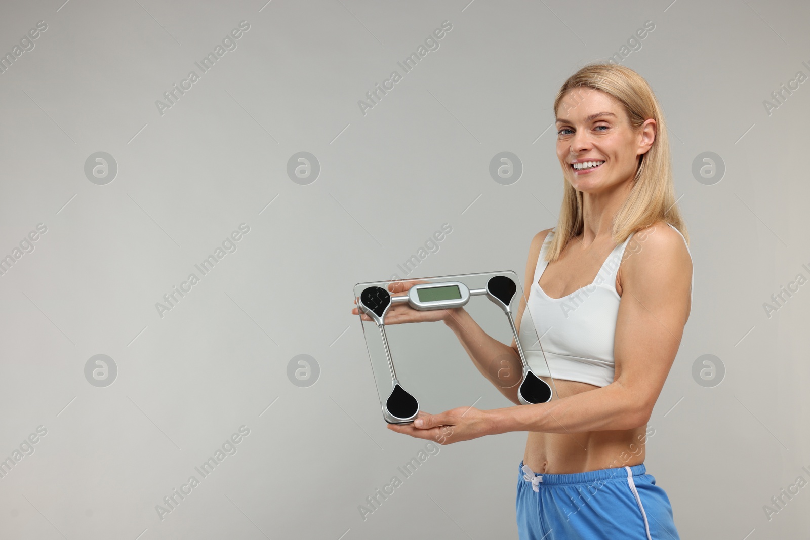 Photo of Slim woman holding scales on grey background, space for text. Weight loss