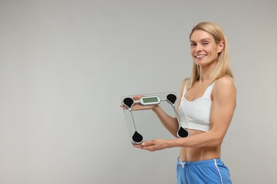 Photo of Slim woman holding scales on grey background, space for text. Weight loss