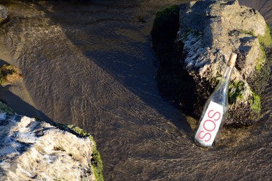 Photo of Glass bottle with SOS message near sea rocks, space for text