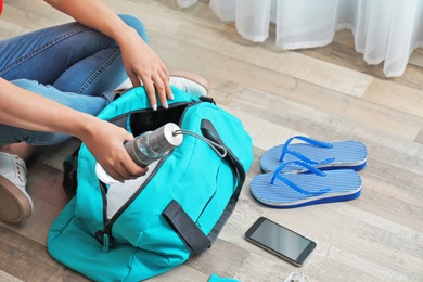 Photo of Young woman packing sports bag on floor