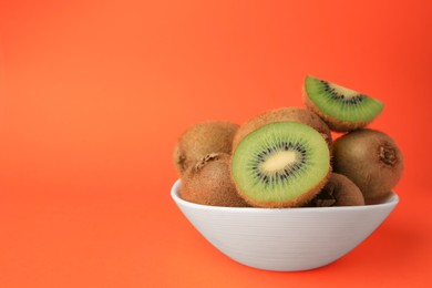 Photo of Bowl of whole and cut fresh ripe kiwis on orange background, space for text