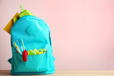 Photo of Bright backpack with different school stationery on wooden table against pink background. Space for text