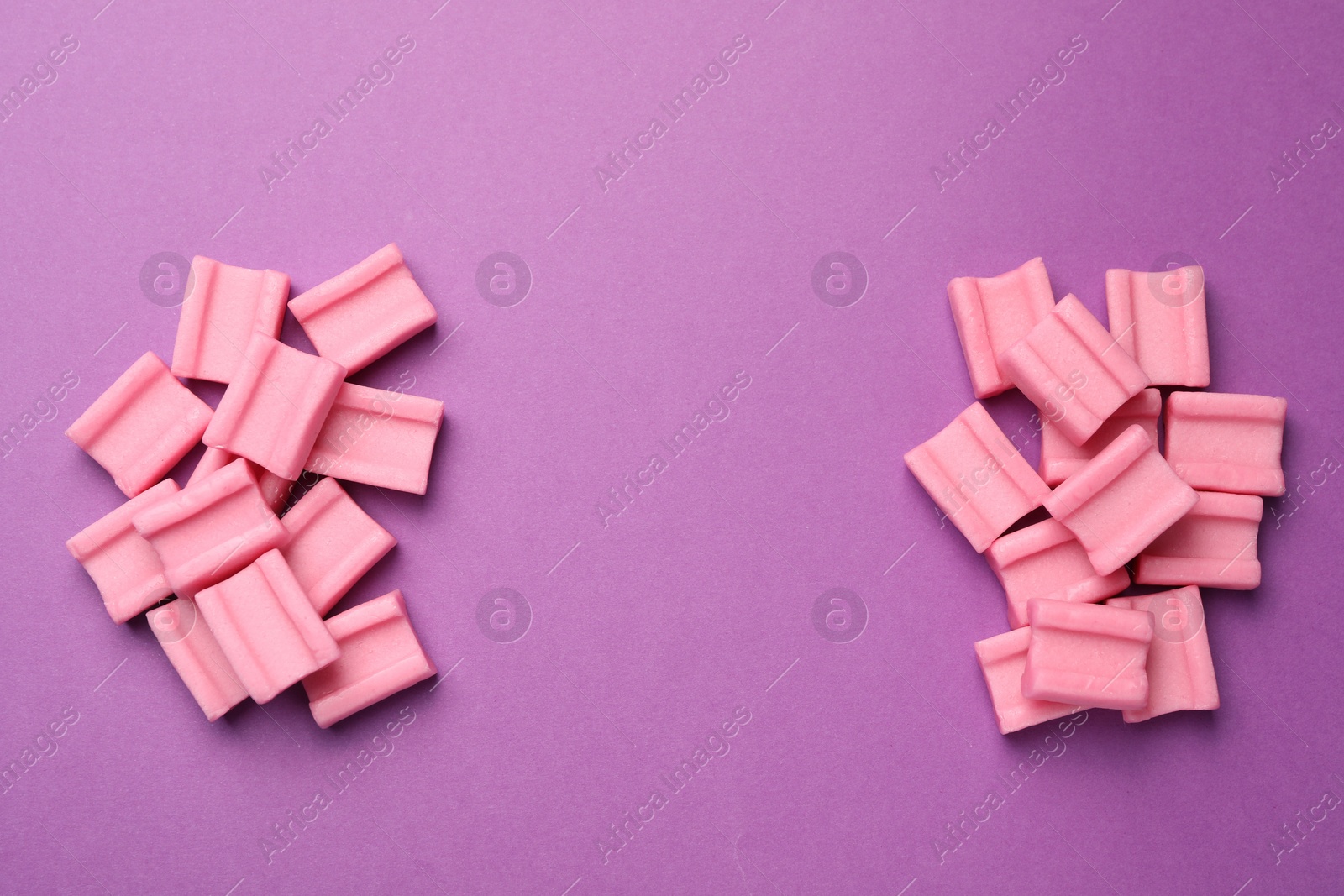 Photo of Tasty pink chewing gums on purple background, flat lay. Space for text