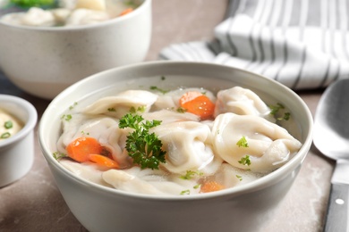 Photo of Bowl of tasty dumplings in broth on table, closeup