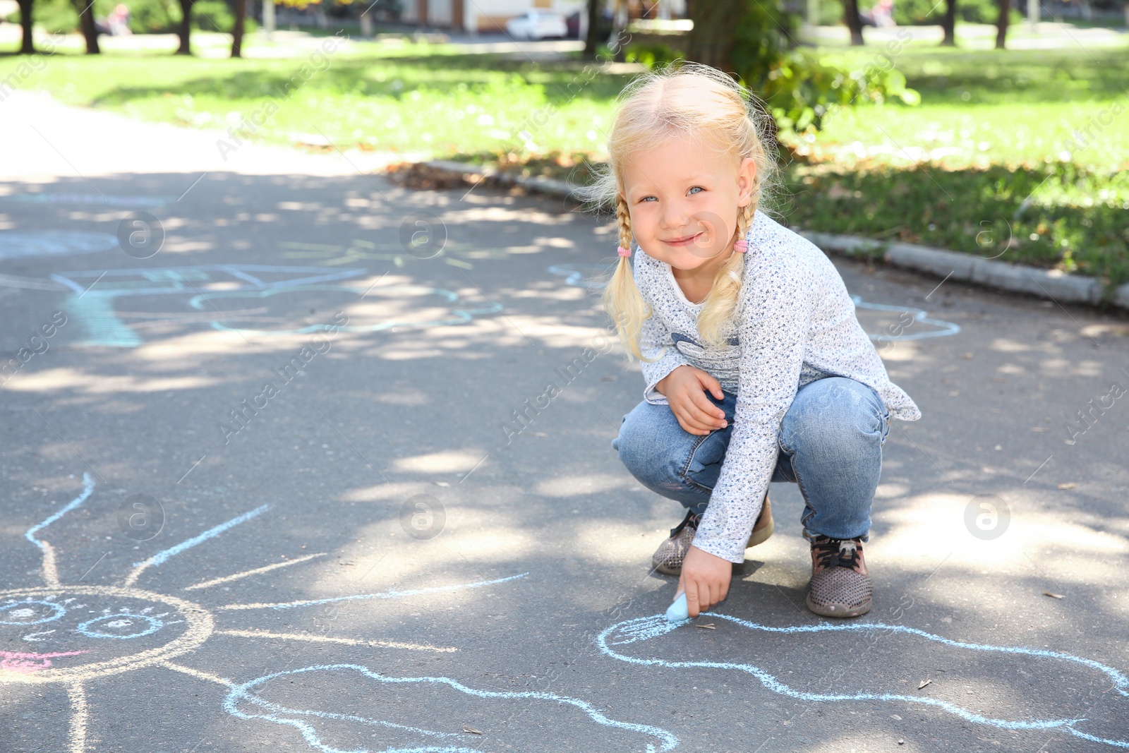 Photo of Little child drawing with colorful chalk on asphalt. Space for text