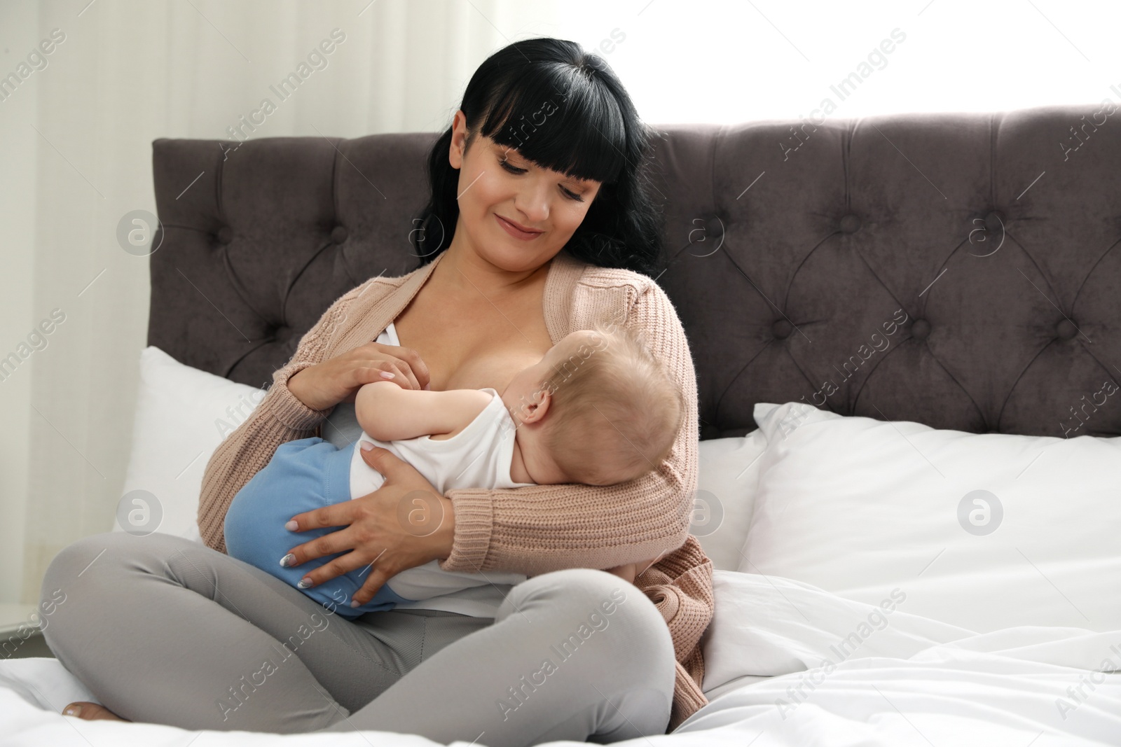 Photo of Woman breastfeeding her little baby on bed indoors