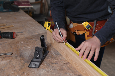 Photo of Professional carpenter measuring wooden plank at workbench, closeup