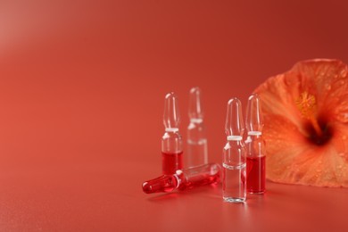 Skincare ampoules and hibiscus flower on coral background. Space for text