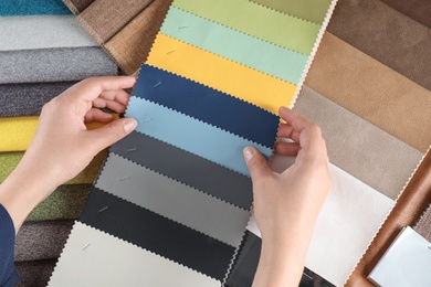 Photo of Young woman choosing among upholstery fabric samples, closeup. Interior design