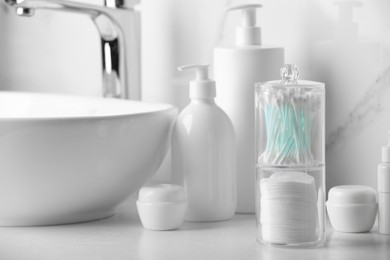 Photo of Containers with cotton swabs and pads near cosmetic products on white countertop in bathroom