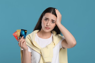 Worried woman with credit cards on light blue background. Debt problem